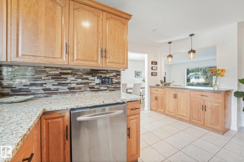 Kitchen featuring light wood cabinetry, stone-finish countertops, stainless steel dishwasher, and mosaic tile backsplash - 16613 90 Avenue Nw, Edmonton, AB - Indoor Photo Showing Kitchen