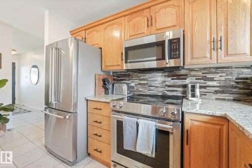 Stainless steel appliances, wood cabinetry, granite countertops, tile flooring, and a mosaic tile backsplash - 16613 90 Avenue Nw, Edmonton, AB - Indoor Photo Showing Kitchen