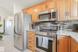 Stainless steel appliances, wood cabinetry, granite countertops, tile flooring, and a mosaic tile backsplash - 