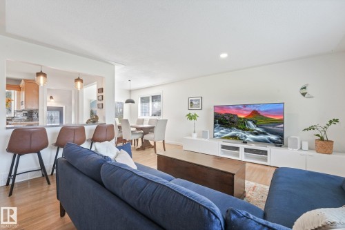 Open-concept living area featuring a navy upholstered sectional sofa, wood-finish flooring throughout, and a wall-mounted entertainment center with white cabinetry - 16613 90 Avenue Nw, Edmonton, AB - Indoor Photo Showing Living Room