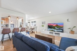 Open-concept living area featuring a navy upholstered sectional sofa, wood-finish flooring throughout, and a wall-mounted entertainment center with white cabinetry - 