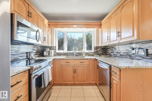 U-shaped kitchen featuring wood cabinetry, stainless steel appliances, a bay window, and a tiled backsplash - 16613 90 Avenue Nw, Edmonton, AB - Indoor Photo Showing Kitchen