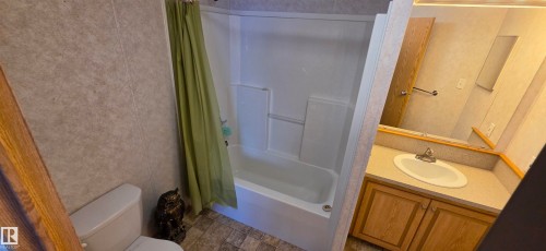 Built-in bathtub with shower surround, vanity with an integrated sink, wood-finish cabinetry, and a wall-mounted mirror - #56 4202 45 St, Wetaskiwin, AB - Indoor Photo Showing Bathroom