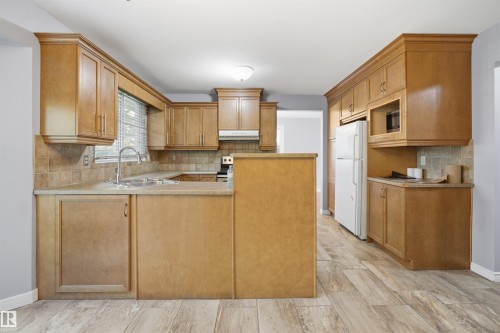 U-shaped kitchen layout featuring wood-finish cabinetry, tile backsplash, laminate countertops, and wood-finish flooring - 3432 Hill View Crescent Nw, Edmonton, AB - Indoor Photo Showing Kitchen