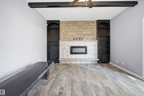 Wood-finish flooring, stone-clad fireplace with integrated electric insert, built-in shelving, and exposed ceiling beams - 3432 Hill View Crescent Nw, Edmonton, AB - Indoor Photo Showing Living Room With Fireplace