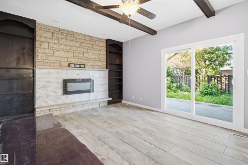 Stone-clad fireplace with an integrated electric insert, flanked by built-in shelving, and exposed ceiling beams - 3432 Hill View Crescent Nw, Edmonton, AB - Indoor With Fireplace