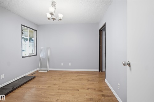 Wood-finish flooring with white trim, contemporary ceiling light fixture, and a window with dark trim - 3432 Hill View Crescent Nw, Edmonton, AB - Indoor Photo Showing Other Room