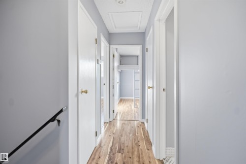 Hallway with wood-finish flooring, light gray walls, white doors with brass hardware, and a ceiling-mounted light fixture - 3432 Hill View Crescent Nw, Edmonton, AB - Indoor Photo Showing Other Room