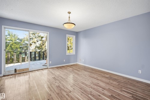 Wood-finish flooring, sliding glass door access to an outdoor deck, recessed window, and overhead semi-flush mount light fixture - 3432 Hill View Crescent Nw, Edmonton, AB - Indoor Photo Showing Other Room