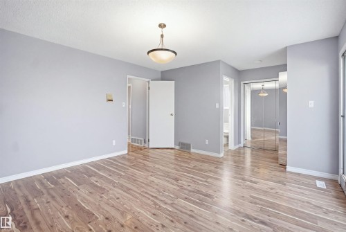 Wood-finish flooring, overhead dome light fixture, white trim, and mirrored closet doors - 3432 Hill View Crescent Nw, Edmonton, AB - Indoor Photo Showing Other Room
