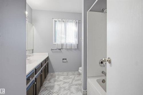 Bathroom featuring a white vanity countertop, dark wood-finish cabinetry, a window with privacy covering, and patterned floor tile - 3432 Hill View Crescent Nw, Edmonton, AB - Indoor Photo Showing Bathroom