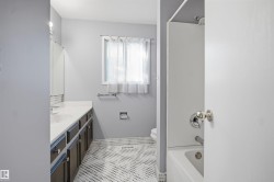 Bathroom featuring a white vanity countertop, dark wood-finish cabinetry, a window with privacy covering, and patterned floor tile - 
