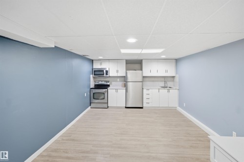 Compact kitchen featuring stainless steel appliances, white cabinetry, light-toned countertops, and a stainless steel sink - 3432 Hill View Crescent Nw, Edmonton, AB - Indoor