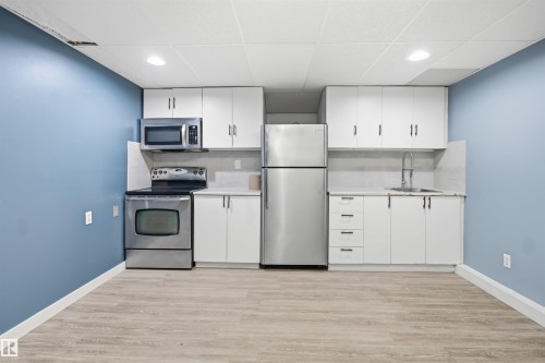 Full kitchen featuring stainless steel appliances, white cabinetry, a sink with a gooseneck faucet, light-toned countertops, and wood-finish flooring - 3432 Hill View Crescent Nw, Edmonton, AB - Indoor Photo Showing Kitchen