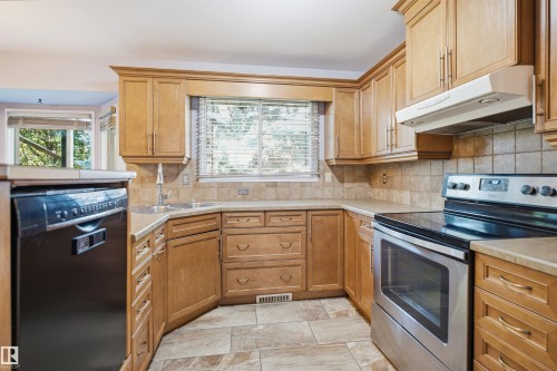 Curved corner kitchen featuring wood cabinetry, stone-look tile flooring, and a stainless steel oven range - 3432 Hill View Crescent Nw, Edmonton, AB - Indoor Photo Showing Kitchen