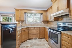 Curved corner kitchen featuring wood cabinetry, stone-look tile flooring, and a stainless steel oven range - 