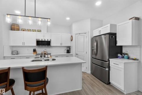 Kitchen featuring a center island, white cabinetry, stainless steel appliances, light wood-finish flooring, and a subway tile backsplash - 91 Hilton Cove, Spruce Grove, AB - Indoor Photo Showing Kitchen With Double Sink With Upgraded Kitchen