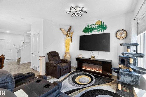 Light-toned wood-finish flooring, a contemporary ceiling light fixture, an electric fireplace with a black console, and white walls - 91 Hilton Cove, Spruce Grove, AB - Indoor With Fireplace