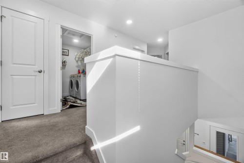 Carpeted stairway with a painted balustrade, leading to a hallway with a white door and a laundry area featuring a washer and dryer - 91 Hilton Cove, Spruce Grove, AB - Indoor Photo Showing Other Room