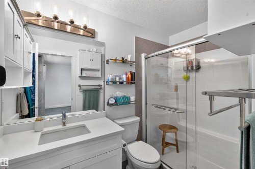 White vanity with integrated sink, brushed nickel lighting fixture, glass-enclosed shower, wall-mounted shelving, and built-in medicine cabinet - 91 Hilton Cove, Spruce Grove, AB - Indoor Photo Showing Bathroom