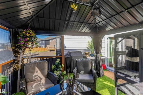 Covered patio with a dark-toned metal roof, featuring a synthetic turf floor and sliding glass door access - 91 Hilton Cove, Spruce Grove, AB - Outdoor With Deck Patio Veranda With Exterior
