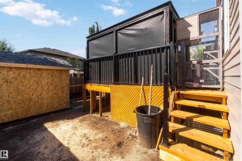 Raised deck with black privacy screening and wood stairs, featuring a side enclosure and adjacent shed with a shingled roof - 91 Hilton Cove, Spruce Grove, AB - Outdoor With Exterior