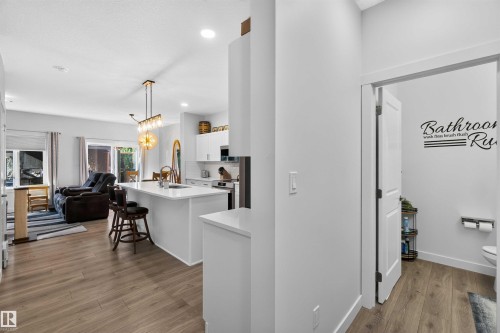 Open-concept kitchen and living area featuring a white island with waterfall edge, wood-finish flooring throughout, pendant lighting, and stainless steel appliances - 91 Hilton Cove, Spruce Grove, AB - Indoor