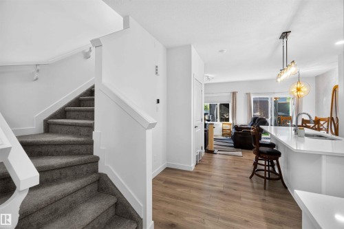 Staircase with gray carpeted treads and white handrails, wood-finish flooring, white kitchen island with countertop, and modern lighting fixtures - 91 Hilton Cove, Spruce Grove, AB - Indoor