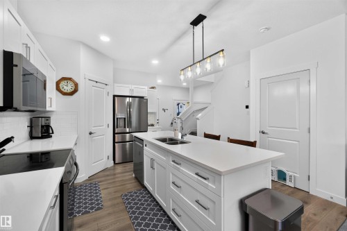 Open-concept kitchen featuring white cabinetry, stainless steel appliances, a large island with an undermount sink, and wood-finish flooring - 91 Hilton Cove, Spruce Grove, AB - Indoor Photo Showing Kitchen With Double Sink With Upgraded Kitchen