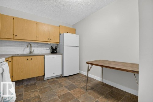 Kitchen featuring wood cabinetry, white subway tile backsplash, a stainless steel sink with a gooseneck faucet, a white dishwasher, and stone-look floor tiles - #804 11027 87 Av Nw, Edmonton, AB - Indoor Photo Showing Kitchen