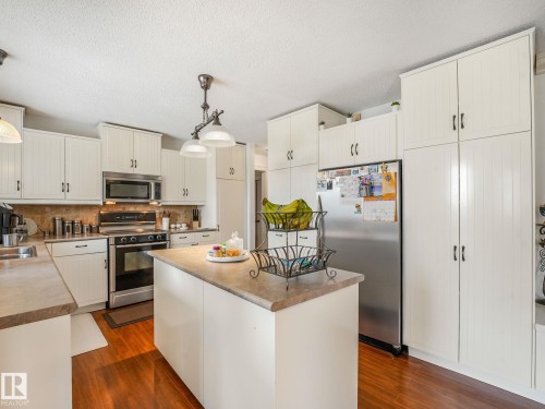 Chef's kitchen featuring white cabinetry with brushed nickel hardware, stainless steel appliances including a gas range and refrigerator, a wood-topped center island with seating, and warm wood-finish flooring throughout - 10912 5 Avenue Sw, Edmonton, AB - Indoor Photo Showing Kitchen With Double Sink