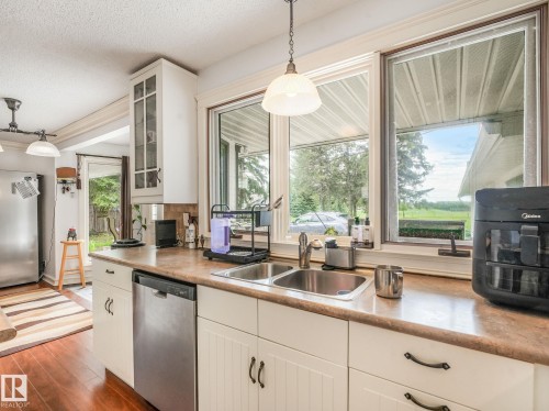 Kitchen featuring a double basin stainless steel sink, stainless steel dishwasher, and wood-finish flooring - 10912 5 Avenue Sw, Edmonton, AB - Indoor Photo Showing Kitchen With Double Sink