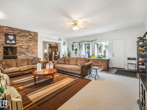 Exposed brick accent wall with a fireplace, ceiling fan with integrated lighting, multiple windows providing natural illumination, and a white entry door - 10912 5 Avenue Sw, Edmonton, AB - Indoor Photo Showing Living Room With Fireplace