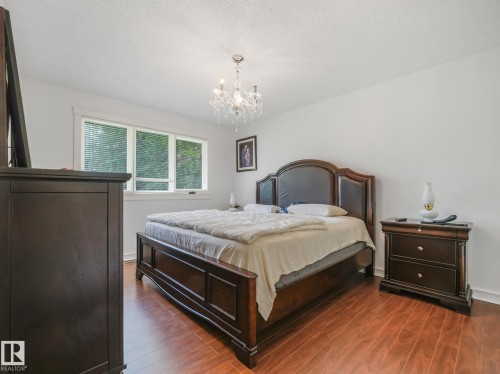 Wood-finish flooring with a crystal chandelier, white walls, and a multi-pane window - 10912 5 Avenue Sw, Edmonton, AB - Indoor Photo Showing Bedroom