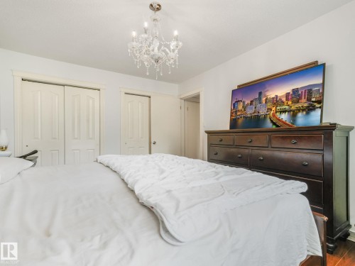 White walls with a crystal chandelier, bi-fold closet doors, and hardwood flooring - 10912 5 Avenue Sw, Edmonton, AB - Indoor Photo Showing Bedroom