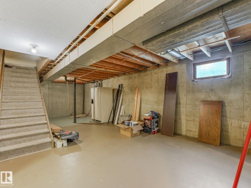 Unfinished lower level with concrete walls, exposed ceiling joists, and a partial carpeted staircase - 10912 5 Avenue Sw, Edmonton, AB - Indoor Photo Showing Basement
