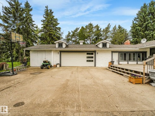 White exterior with a modern garage door, multiple dormer windows, a concrete driveway, and a spacious wood deck - 10912 5 Avenue Sw, Edmonton, AB - Outdoor
