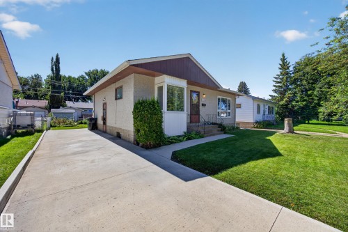 Stucco exterior with a bay window, concrete driveway, front lawn, mature trees, and established landscaping - 5207 48 Avenue, Leduc, AB - Outdoor