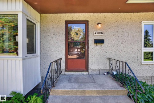 Textured exterior facade, concrete entry steps, wrought iron handrails, bay window, and a red entry door - 5207 48 Avenue, Leduc, AB - Outdoor With Exterior