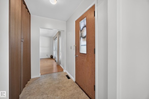 Entryway featuring a wood-finish door with decorative glass insert, neutral tone flooring, and an integrated storage unit with patterned doors - 5207 48 Avenue, Leduc, AB - Indoor Photo Showing Other Room