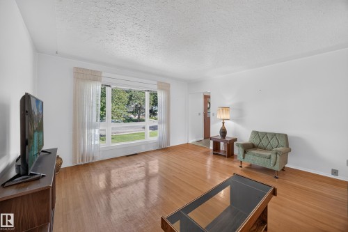 Hardwood-finish flooring, white painted walls, and a large picture window with white trim - 5207 48 Avenue, Leduc, AB - Indoor Photo Showing Living Room