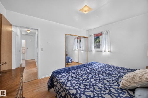 Hardwood flooring, mirrored closet doors, ceiling light fixture, white walls, and a window with natural light - 5207 48 Avenue, Leduc, AB - Indoor Photo Showing Bedroom