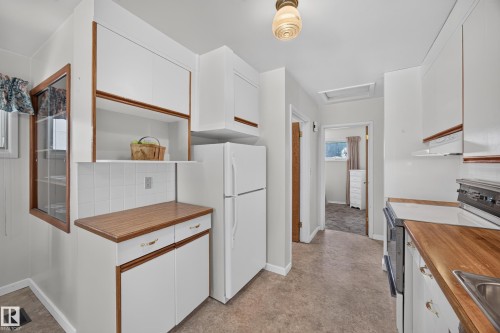 White cabinetry with wood-finish trim, wood-finish countertops, tiled backsplash, and permanent overhead light fixture - 5207 48 Avenue, Leduc, AB - Indoor Photo Showing Kitchen