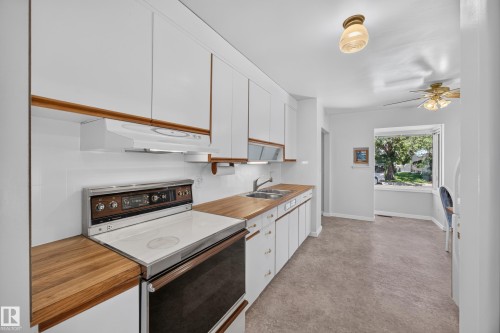 White cabinetry with wood-finish trim, wood-finish countertops, and a dual basin sink - 5207 48 Avenue, Leduc, AB - Indoor Photo Showing Kitchen With Double Sink