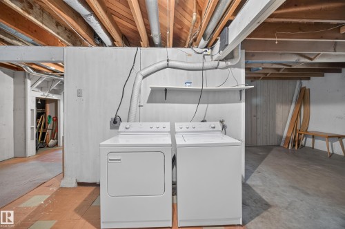Utility area featuring exposed wood ceiling joists, durable flooring, a white washer, a white dryer, and a wall-mounted shelf - 5207 48 Avenue, Leduc, AB - Indoor Photo Showing Laundry Room