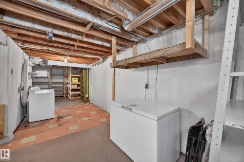 Unfinished basement with exposed ceiling joists, concrete walls, and a utility area featuring a washing machine - 5207 48 Avenue, Leduc, AB - Indoor Photo Showing Basement