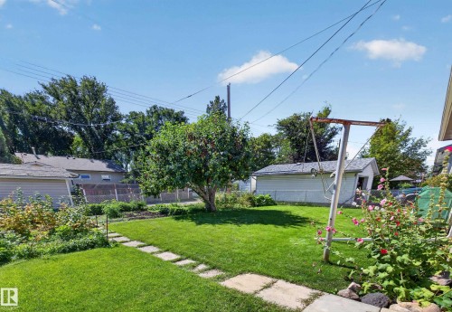 Expansive lawn with a mature tree, bordered by a square paver pathway and garden beds - 5207 48 Avenue, Leduc, AB - Outdoor