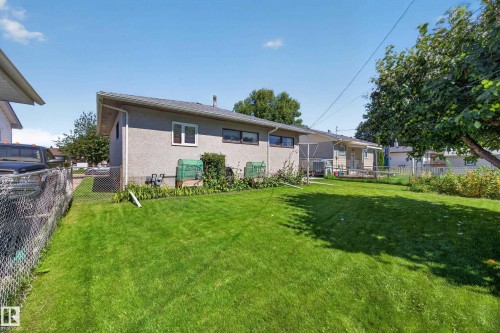 Expansive rear yard featuring a manicured lawn, established landscaping, mature trees, and a chain-link fence - 5207 48 Avenue, Leduc, AB - Outdoor