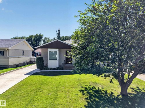 Rendered exterior featuring a bay window, concrete driveway, front yard with green lawn, and mature trees - 5207 48 Avenue, Leduc, AB - Outdoor