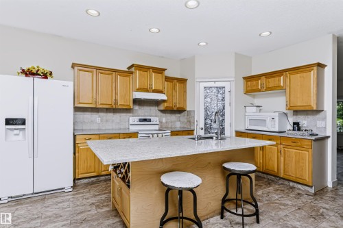 Wood-finish cabinetry, light-toned stone countertops, and a tiled backsplash - 1720 Robertson Place Sw, Edmonton, AB - Indoor Photo Showing Kitchen With Double Sink